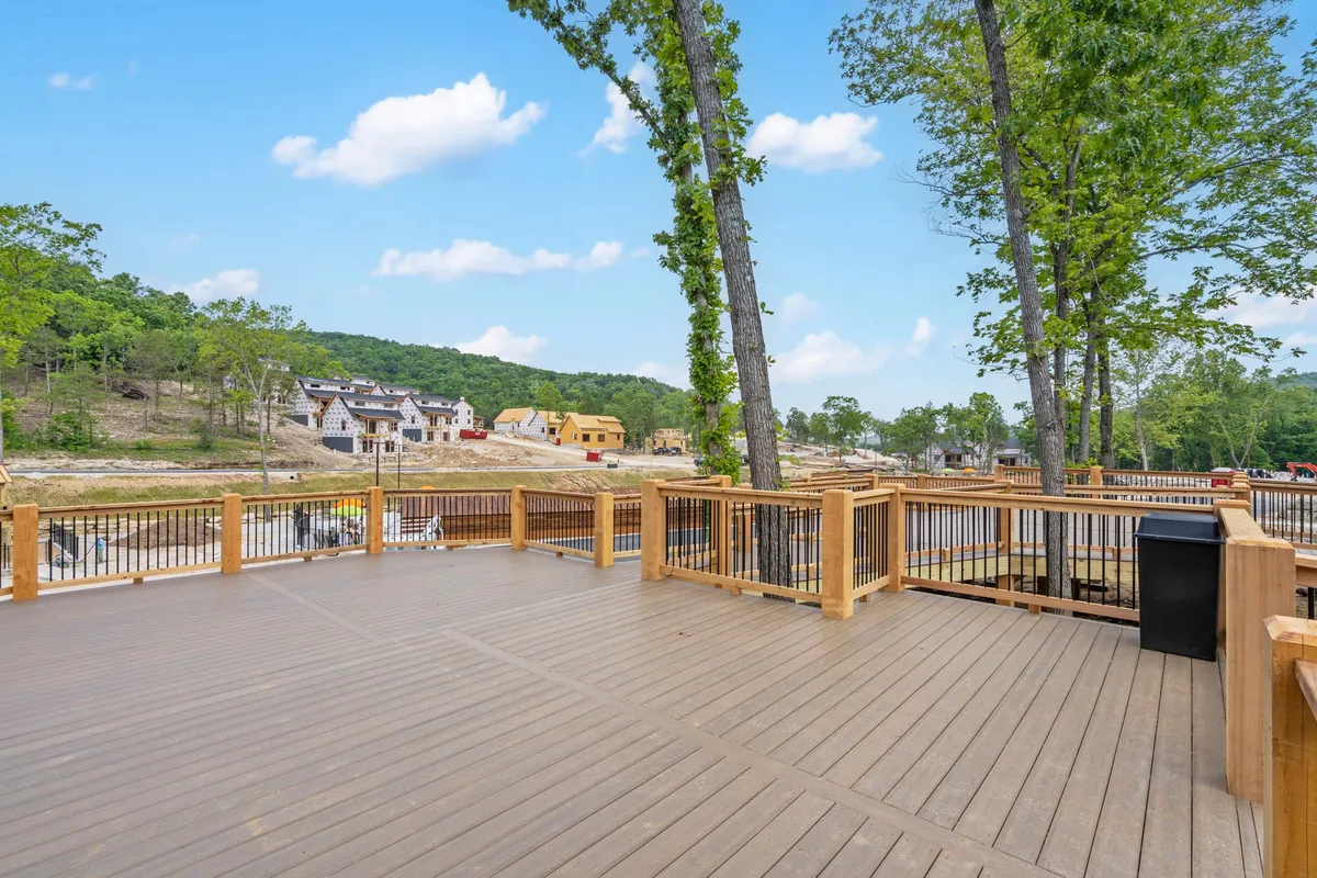 A spacious wooden deck nestled among mature trees offers tranquil views of Timber Lake and the surrounding natural setting. Comfortable outdoor seating invites guests to enjoy a morning coffee, while the warm light suggests the possibility of both sunrise and sunset experiences. The deck is framed by greenery, with glimpses of other houses nearby, reinforcing the retreat's communal yet private vibe.