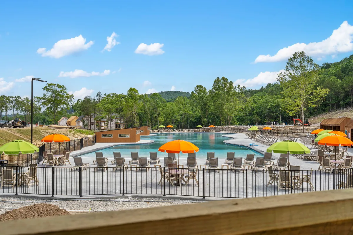 A vibrant scene of a swimming pool with colorful umbrellas, lounge chairs, and trees in the background. The mood is cheerful and relaxed, suggesting a family-friendly spot for swimming, sunbathing, and gatherings.