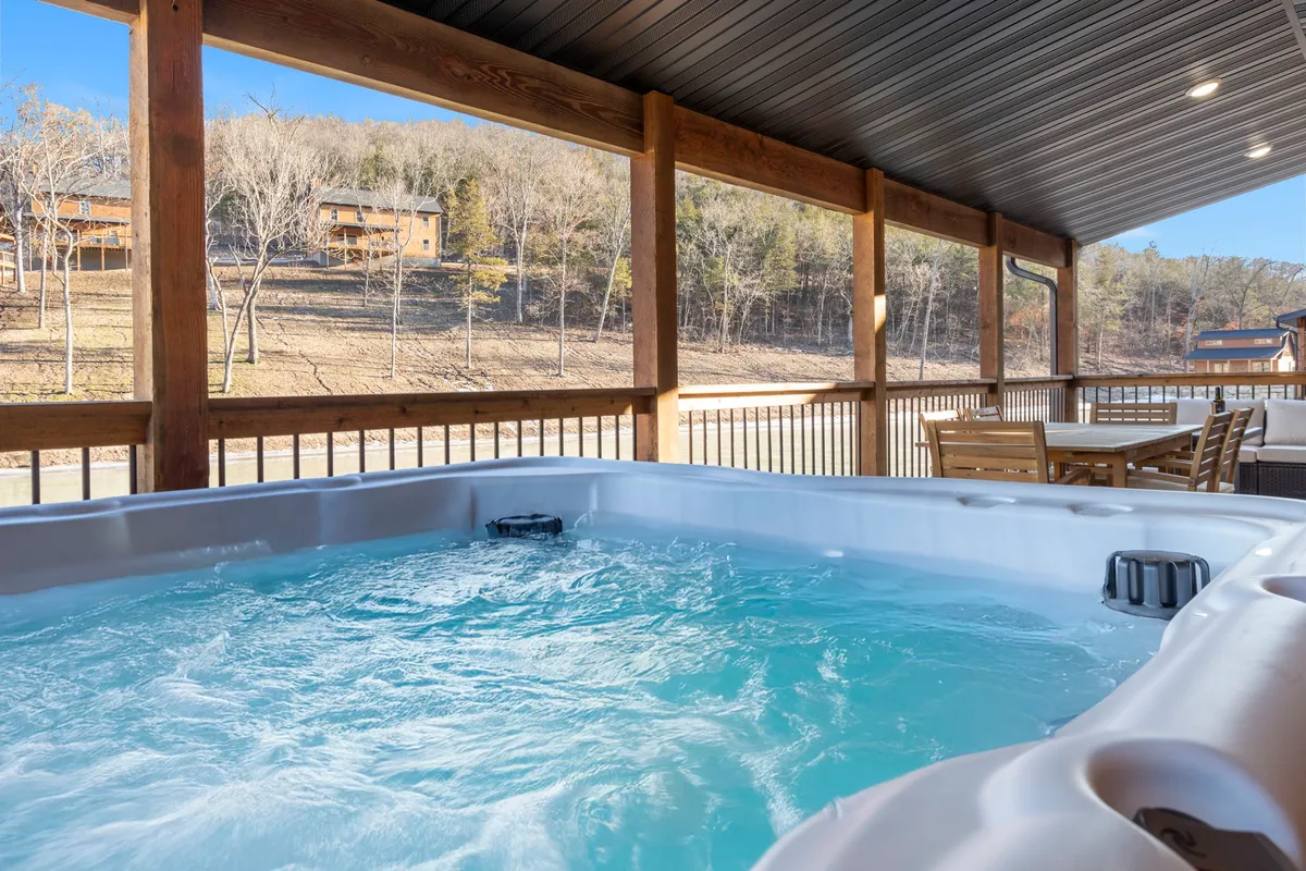 This image features a tranquil hot tub surrounded by a wooden railing and outdoor seating, set against a backdrop of lush greenery. The scene exudes relaxation and invites guests to imagine soaking under the stars or enjoying a morning coffee while immersed in nature.