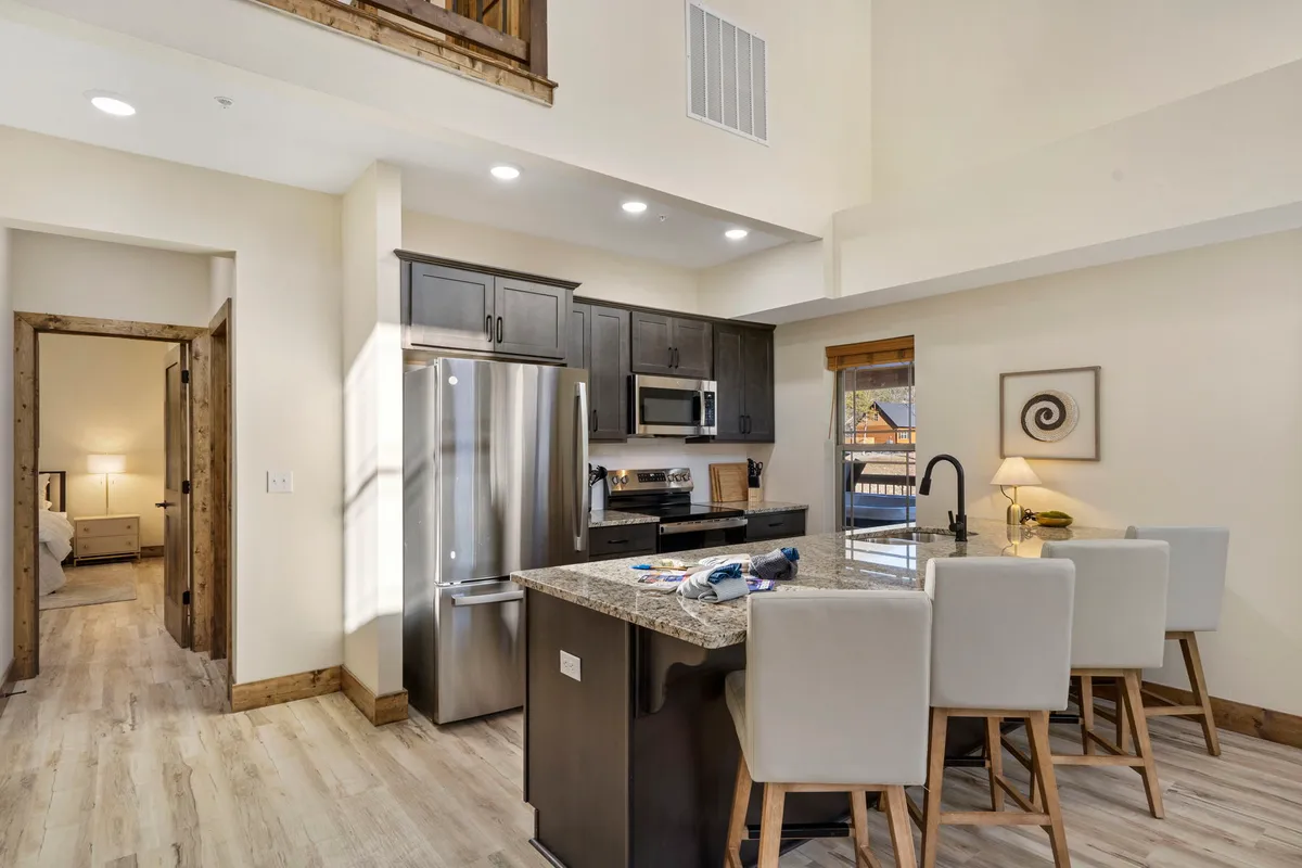 A modern kitchen featuring a spacious island bar with bar stools, stainless steel appliances, and elegant granite countertops. The open design encourages socializing and group cooking, serving as the heart of culinary adventures.