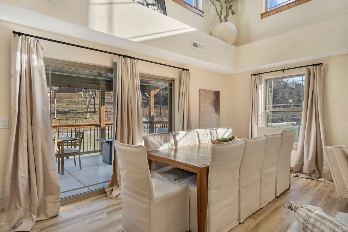 A cozy dining area with a large wooden table positioned beside expansive windows draped in curtains, inviting gatherings for meals and conversation. The setup is perfect for both festive celebrations and casual breakfasts.