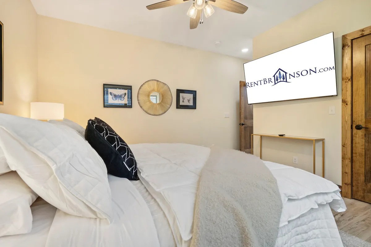 A welcoming bedroom with a comfortable bed dressed in white bedding and decorative pillows, a wall-mounted television, and framed artwork. The space exudes warmth and provides a sense of personal haven to relax and recharge.