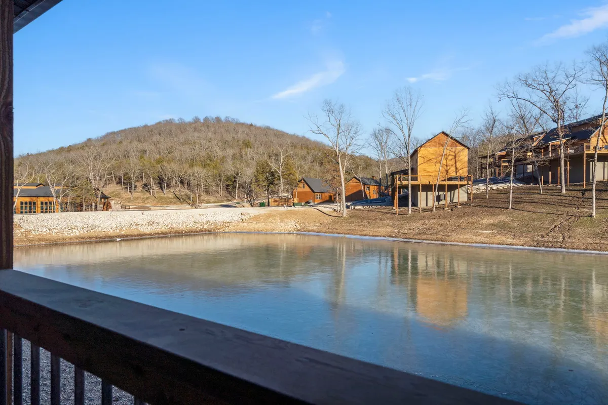 A peaceful lake reflects the sunrise, surrounded by mountains and several wooden cabins. The scene includes opportunities for fishing, nature walks, and outdoor gatherings, with an overall serene and natural ambiance.