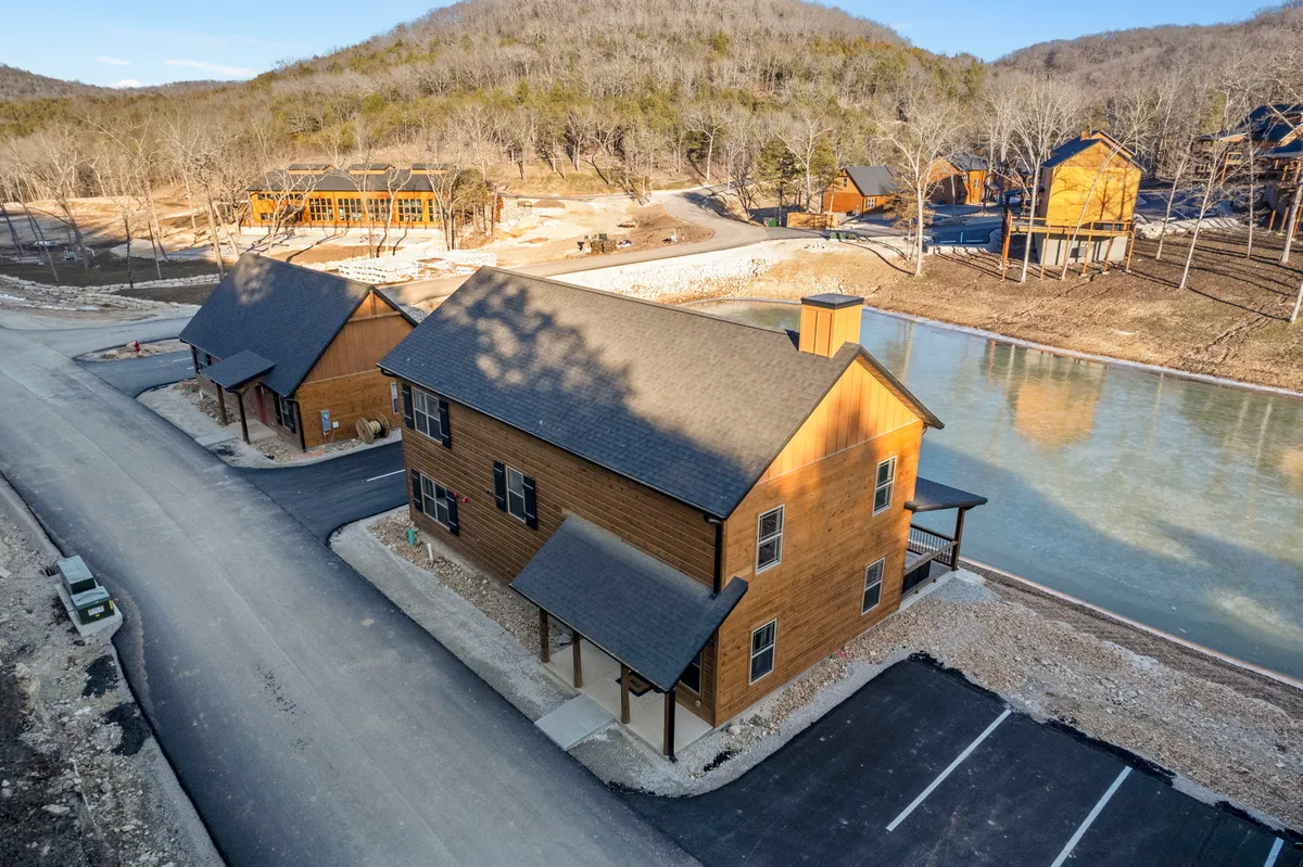 This serene exterior image showcases two wooden cabins set along the calm shore of a lake, surrounded by lush trees. The reflection of the sunset on the water creates a peaceful atmosphere ideal for family gatherings, outdoor barbecues, and fishing.
