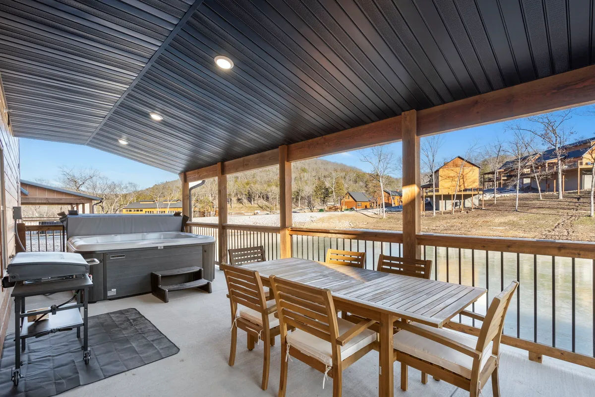 A spacious wooden deck overlooking scenic mountain views, featuring a hot tub, a family-sized dining table, and sturdy railings. The scene is set for outdoor dining, with spaces for both grilling and gathering, all illuminated by soft natural light.