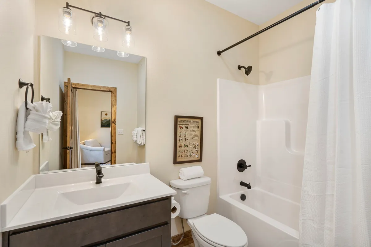 A spacious, inviting bathroom featuring a modern vanity with sink, a large mirror, luxurious bathtub, towel rack, and framed artwork. The ambiance is fresh, bright, and perfect for unwinding routines.
