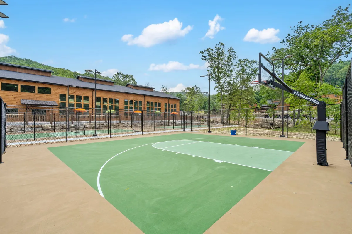 A vibrant basketball court framed by leafy trees, with a visible hoop and an adjacent building in the background. The open design invites guests to enjoy casual or competitive play in a natural, energetic setting.